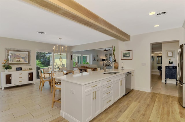 kitchen with visible vents, a peninsula, a sink, appliances with stainless steel finishes, and beamed ceiling