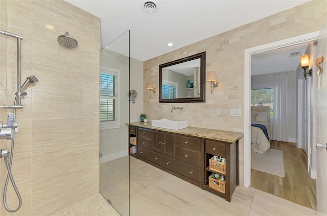 full bathroom with visible vents, a walk in shower, tile walls, and vanity