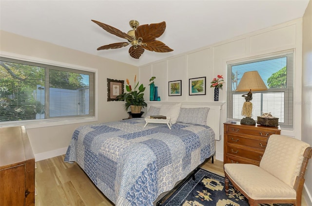 bedroom featuring a decorative wall, baseboards, light wood-type flooring, and a ceiling fan