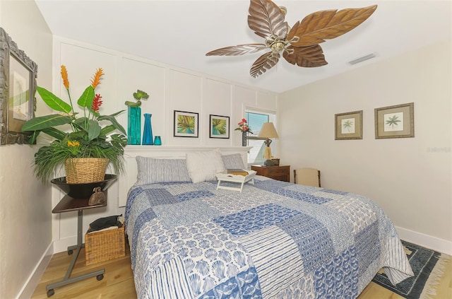 bedroom featuring visible vents, wood finished floors, a decorative wall, baseboards, and ceiling fan