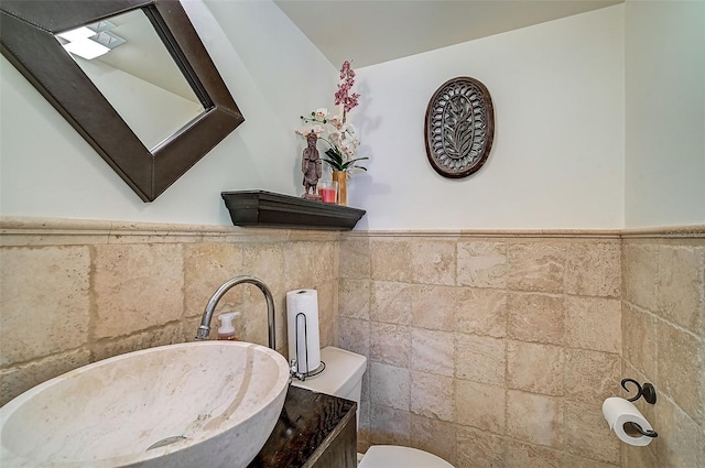 bathroom featuring tile walls, toilet, a wainscoted wall, and a sink