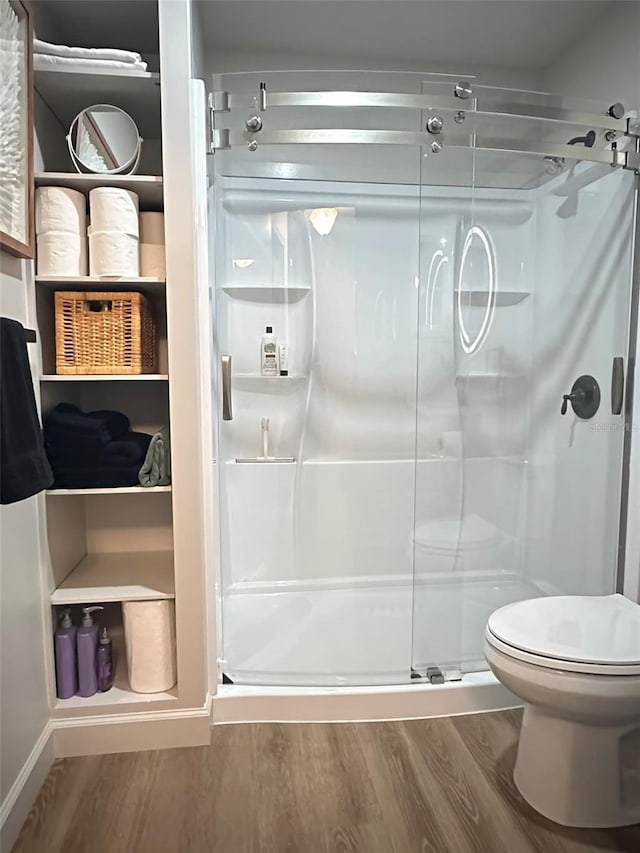 bathroom with toilet, wood finished floors, and a stall shower