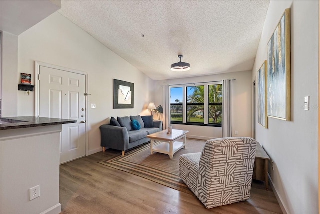 living room with vaulted ceiling, wood finished floors, baseboards, and a textured ceiling