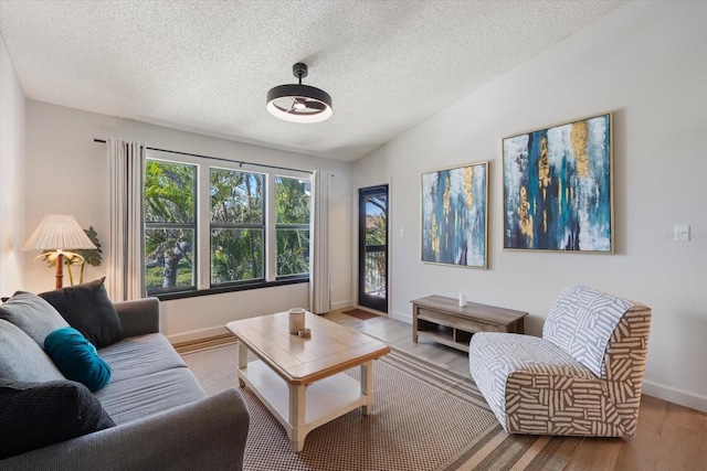 living room with lofted ceiling, wood finished floors, baseboards, and a textured ceiling