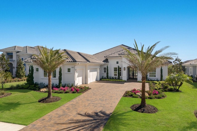 mediterranean / spanish-style house featuring a front yard, stucco siding, a garage, a tiled roof, and decorative driveway