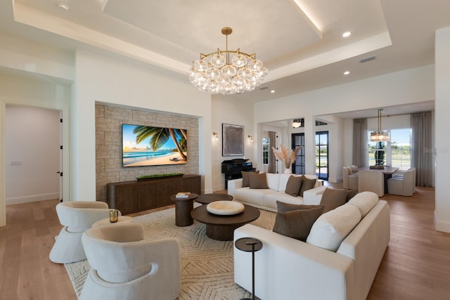 living area with a tray ceiling, baseboards, a notable chandelier, and wood finished floors