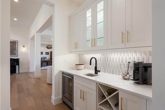 bar featuring beverage cooler, a sink, wood finished floors, decorative backsplash, and baseboards