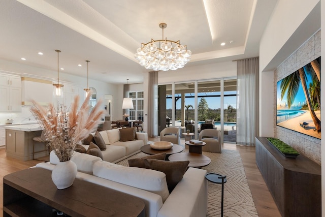 living area with recessed lighting, a notable chandelier, light wood-style flooring, and a tray ceiling