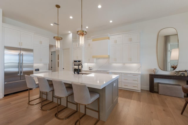 kitchen featuring a center island with sink, built in refrigerator, white cabinetry, black electric cooktop, and a sink