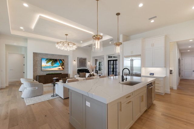 kitchen with open floor plan, light wood-type flooring, stainless steel appliances, a raised ceiling, and a sink