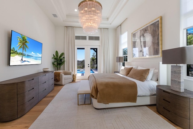 bedroom featuring visible vents, light wood-type flooring, a tray ceiling, an inviting chandelier, and access to outside