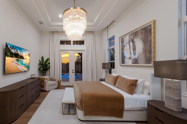 bedroom featuring a tray ceiling, wood finished floors, french doors, an inviting chandelier, and access to exterior