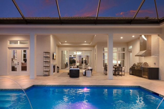 pool at dusk with a patio, french doors, a grill, exterior kitchen, and an outdoor pool