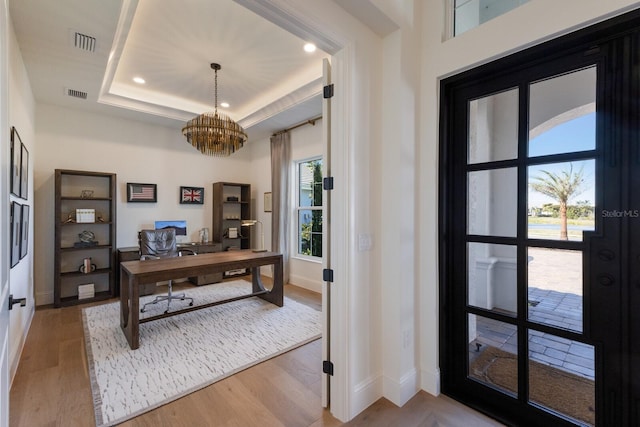 office featuring wood finished floors, baseboards, visible vents, a raised ceiling, and a chandelier