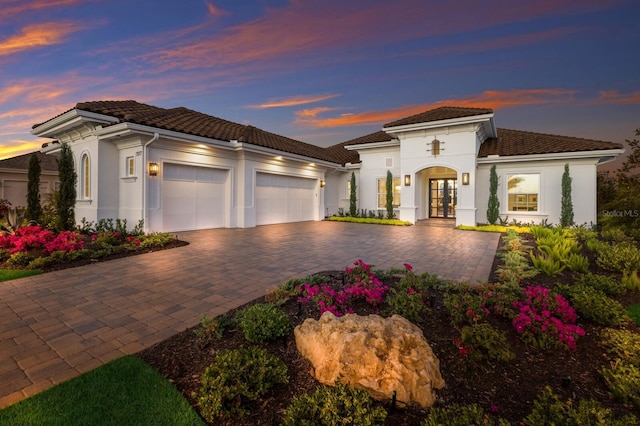 mediterranean / spanish house featuring an attached garage, stucco siding, french doors, a tiled roof, and decorative driveway