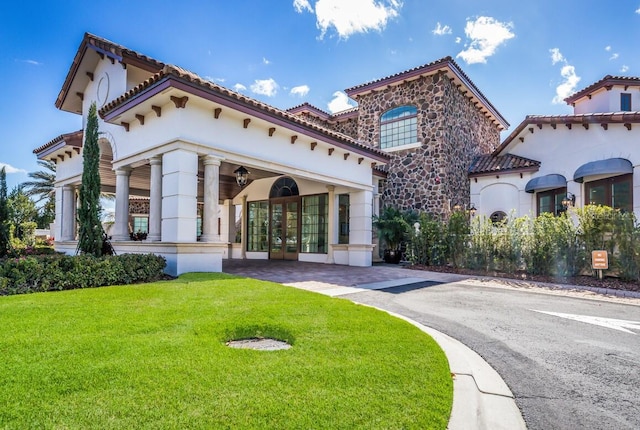 mediterranean / spanish home featuring a front lawn, a tiled roof, french doors, and stucco siding