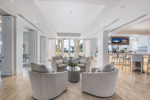 living area featuring a raised ceiling, recessed lighting, light wood-type flooring, and a wealth of natural light