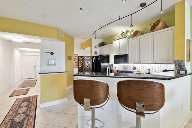 kitchen featuring dark countertops, tasteful backsplash, light tile patterned floors, a peninsula, and black appliances