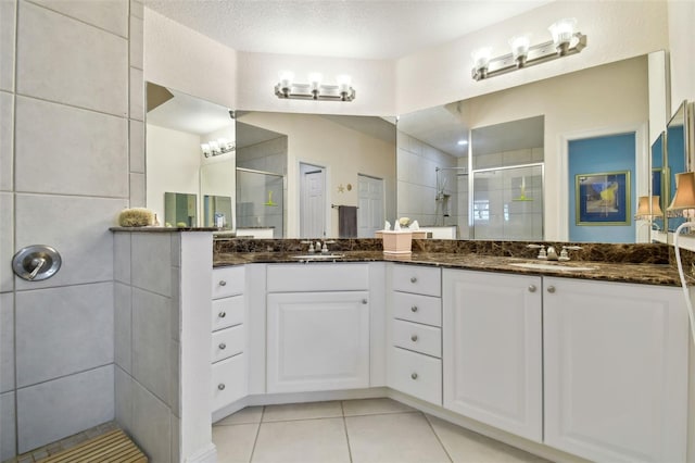 bathroom with tile patterned floors, double vanity, a stall shower, and a sink