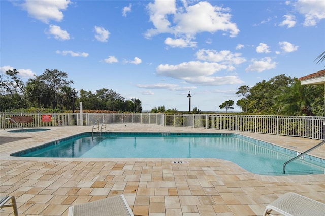 community pool with a patio area, fence, and a hot tub