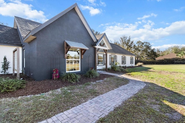 view of side of property featuring stucco siding, a lawn, and roof with shingles