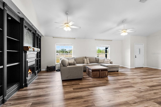 living room with vaulted ceiling, a glass covered fireplace, a healthy amount of sunlight, and wood finished floors