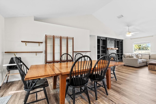 dining room featuring a ceiling fan, visible vents, light wood finished floors, lofted ceiling, and a lit fireplace