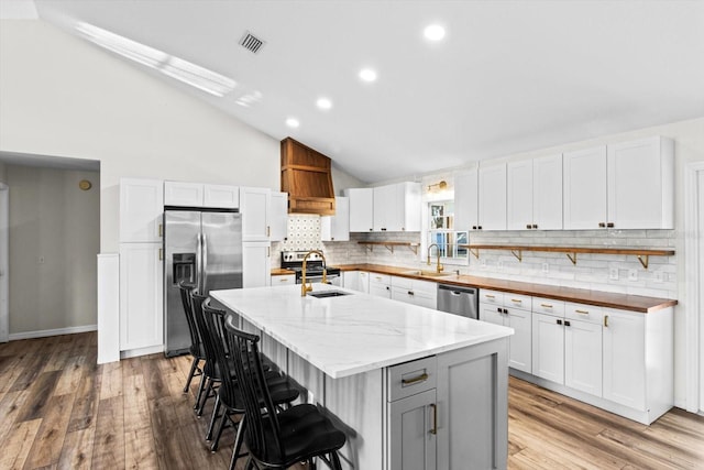 kitchen featuring visible vents, a breakfast bar, white cabinetry, appliances with stainless steel finishes, and vaulted ceiling