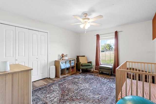 bedroom featuring a crib, wood finished floors, a closet, and a ceiling fan