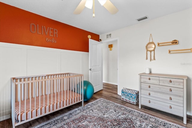 bedroom with a crib, wood finished floors, visible vents, and wainscoting