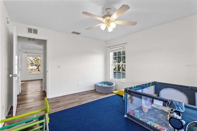 recreation room featuring ceiling fan, wood finished floors, visible vents, and baseboards