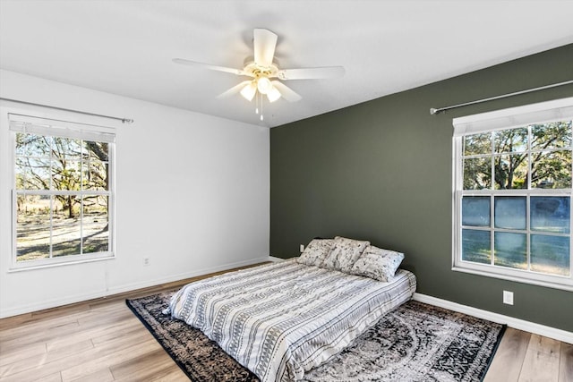 bedroom with multiple windows, a ceiling fan, baseboards, and wood finished floors