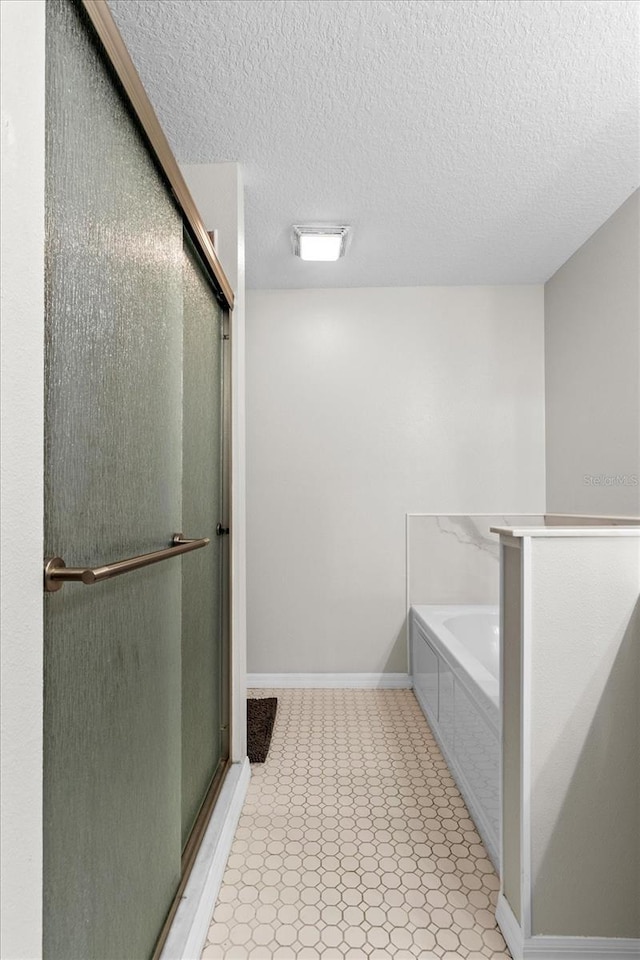 bathroom with a garden tub, baseboards, a shower stall, and a textured ceiling