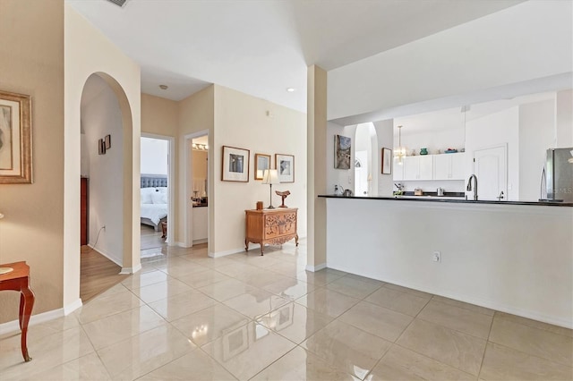 kitchen with dark countertops, freestanding refrigerator, arched walkways, white cabinets, and a sink