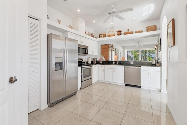 kitchen with dark countertops, light tile patterned flooring, white cabinets, stainless steel appliances, and a sink