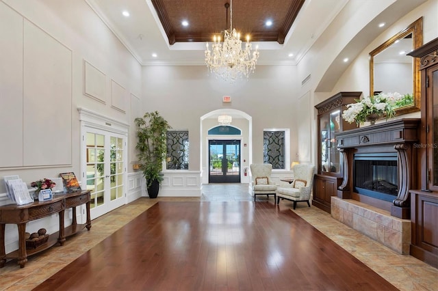 foyer entrance with a tray ceiling, wood finished floors, french doors, arched walkways, and a tile fireplace