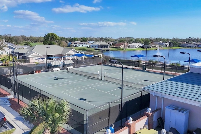 view of tennis court featuring fence, a water view, and a residential view