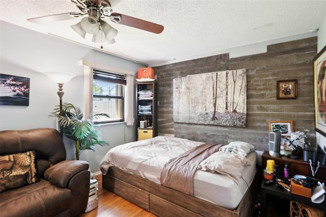 bedroom with a ceiling fan, a textured ceiling, wood finished floors, wood walls, and an accent wall