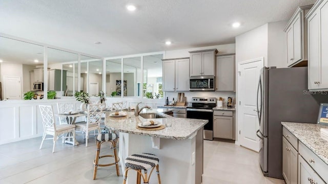 kitchen with a sink, light stone counters, appliances with stainless steel finishes, and gray cabinets