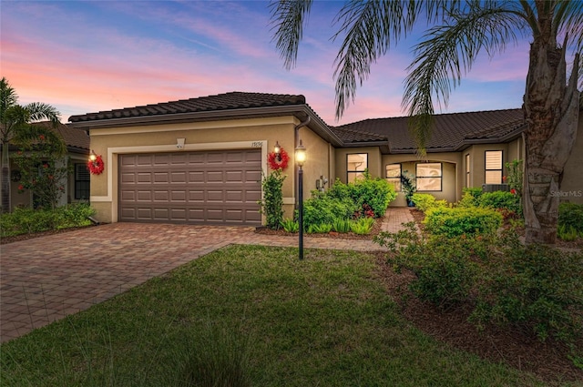 view of front of property featuring stucco siding, a tile roof, decorative driveway, and a garage