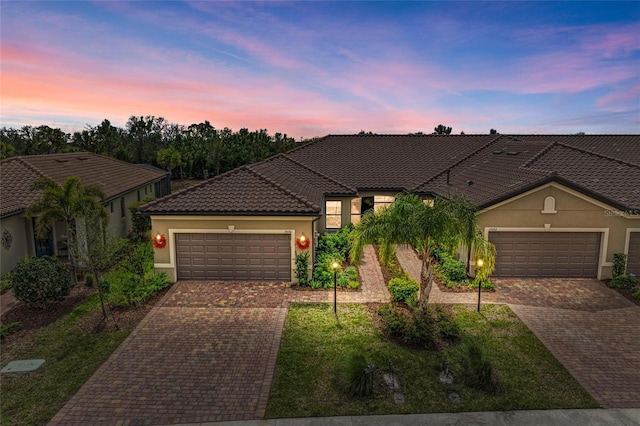 view of front of home featuring decorative driveway, a tile roof, an attached garage, and stucco siding