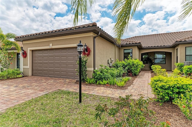 mediterranean / spanish-style home with a tile roof, decorative driveway, a garage, and stucco siding