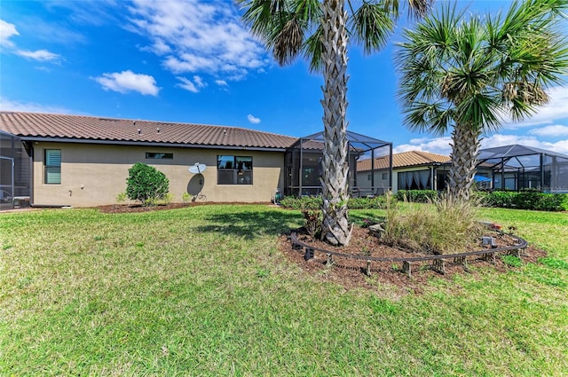 back of property with stucco siding, a yard, glass enclosure, and a tiled roof