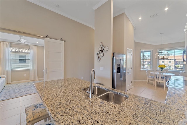 kitchen featuring light tile patterned floors, ornamental molding, a sink, a barn door, and stainless steel fridge