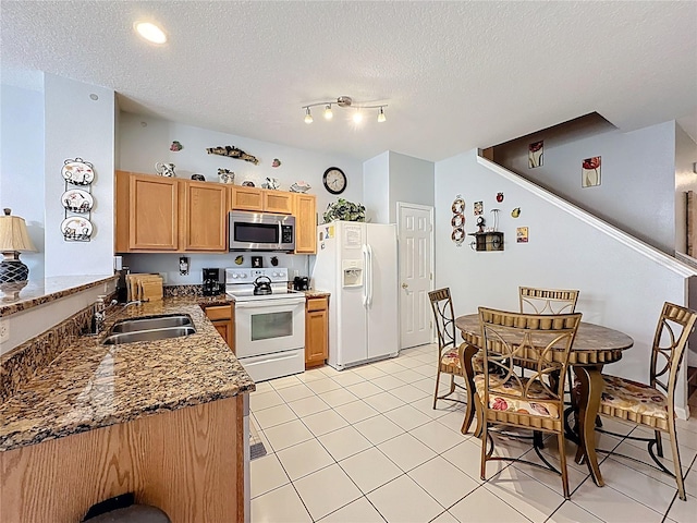 kitchen featuring a textured ceiling, white appliances, stone counters, and a sink