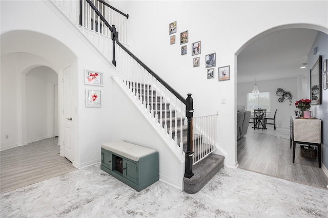 staircase with baseboards, arched walkways, marble finish floor, and a towering ceiling