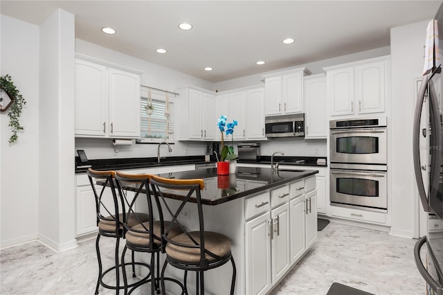 kitchen featuring a kitchen bar, white cabinets, a center island with sink, and appliances with stainless steel finishes