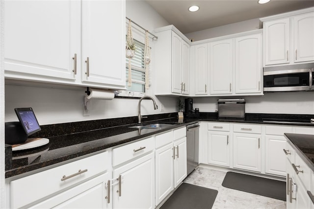 kitchen featuring white cabinets, appliances with stainless steel finishes, dark stone counters, and a sink