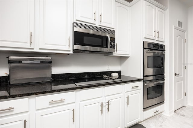 kitchen with dark stone countertops, visible vents, appliances with stainless steel finishes, white cabinetry, and marble finish floor