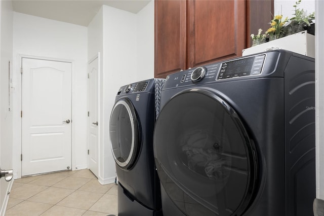 clothes washing area featuring washer and clothes dryer, light tile patterned floors, and cabinet space